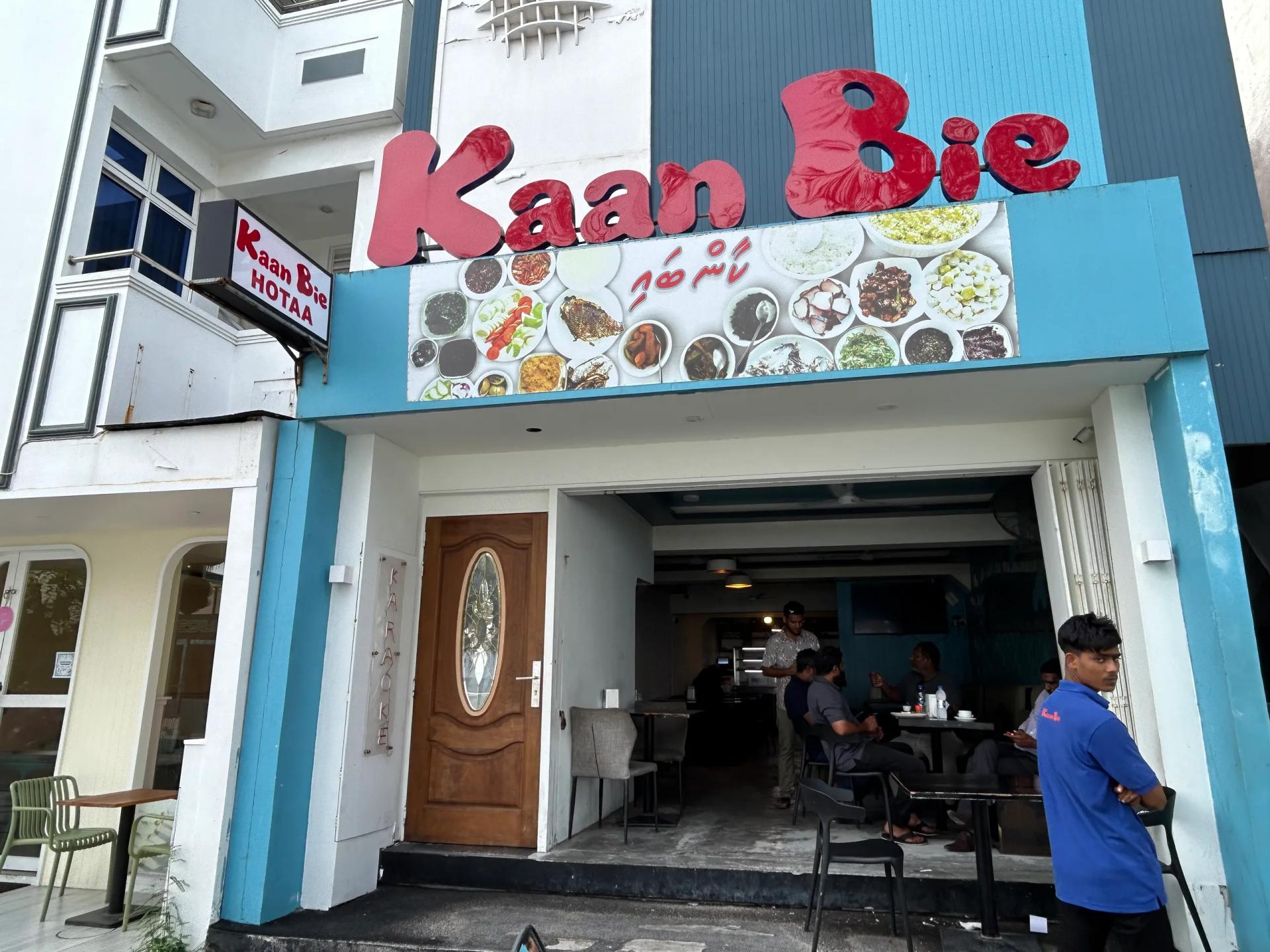 Kaan Bie Hotaa entrance with a food-photo banner overhead and diners seated inside the dim interior