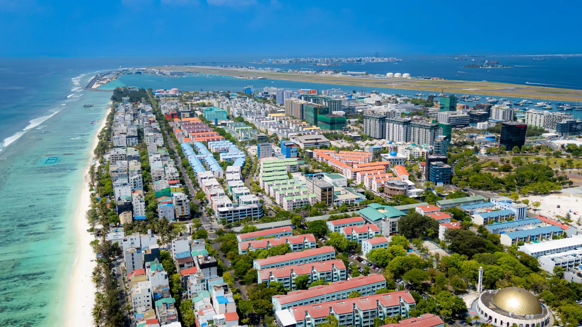Aerial view of Hulhumalé's long beach and housing blocks, with Malé on the horizon
