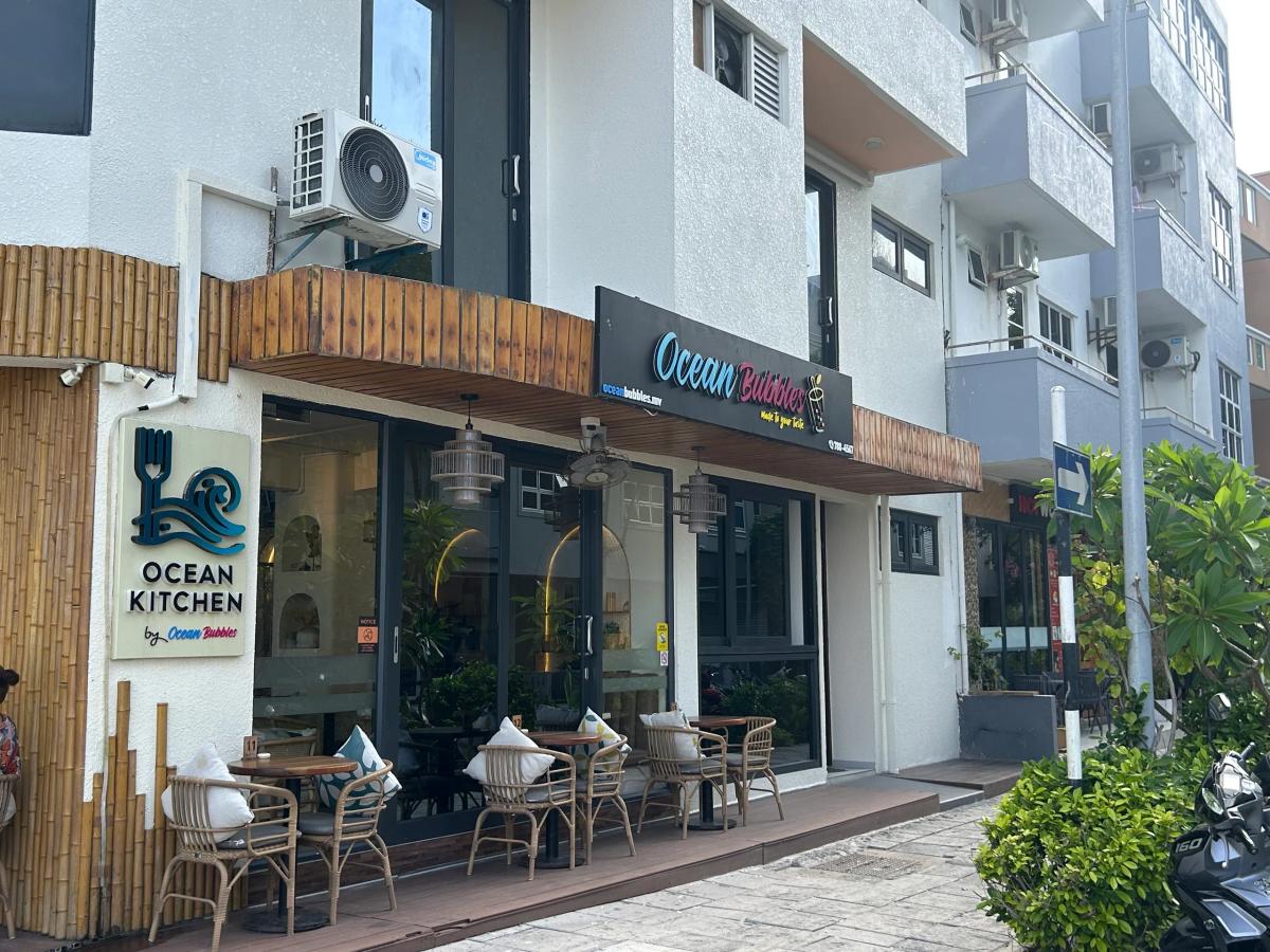 Outdoor terrace seating with rattan chairs at Ocean Kitchen by Ocean Bubbles, signage above the entrance