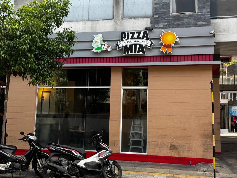 Pizza Mia corner shopfront sign reading Qualita Originale above tan-panelled glass windows, motorbikes parked outside