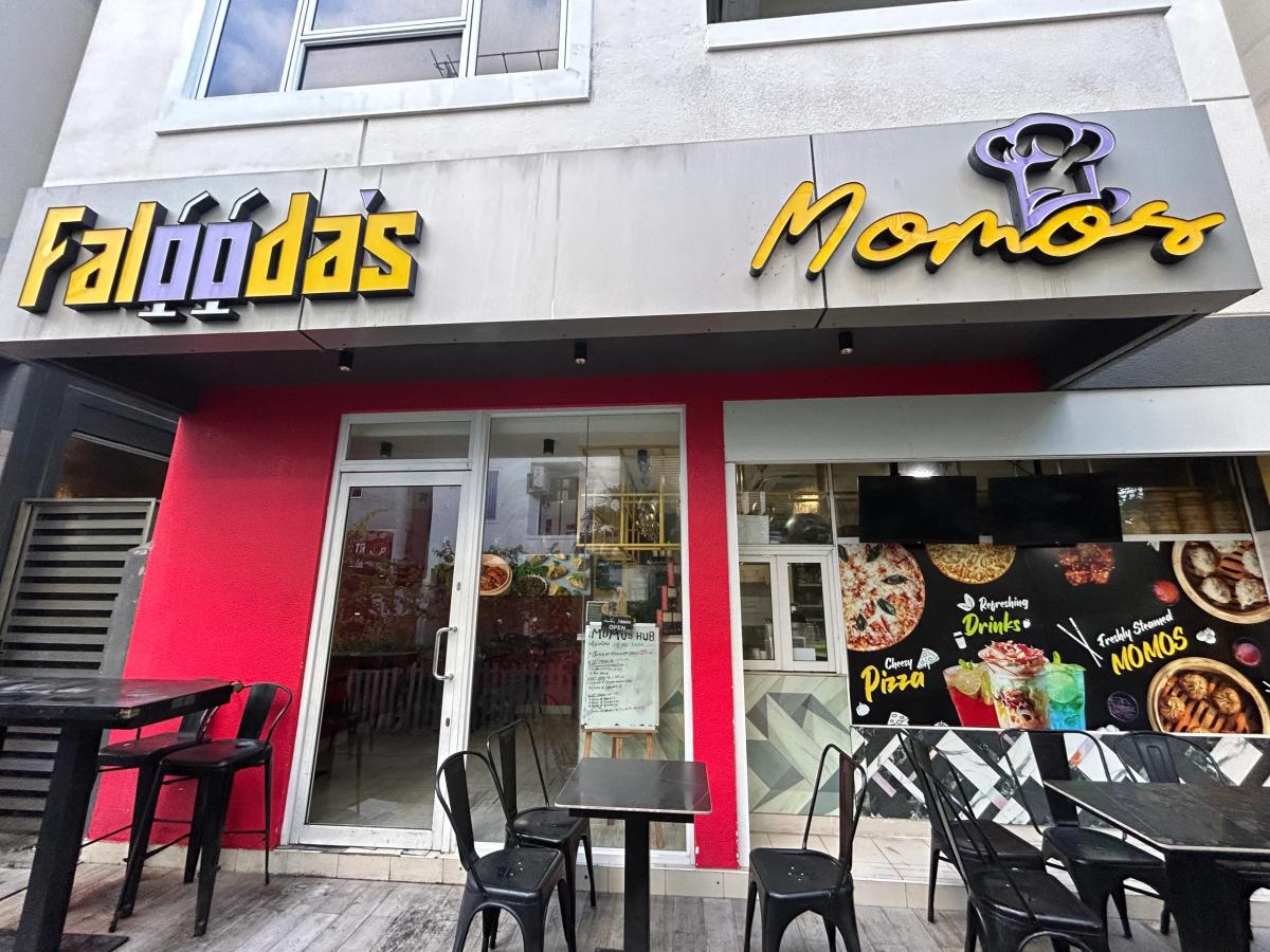 Red facade with neon Faloodas and Momos signs above an outdoor seating area with black tables
