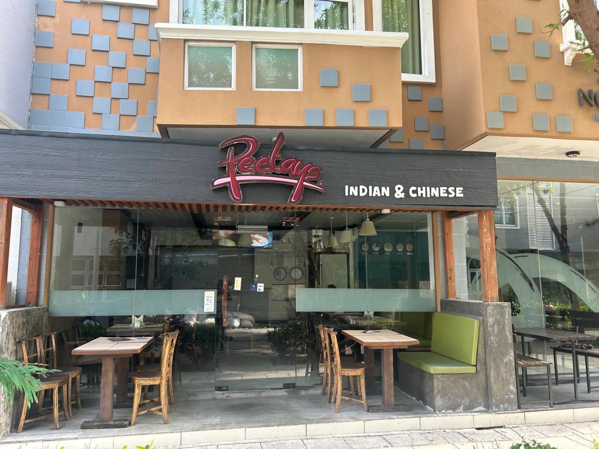 Open storefront of Peetays Indian & Chinese restaurant with outdoor wooden tables and a green banquette