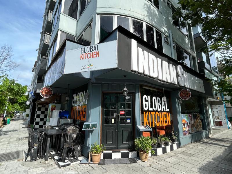 Corner entrance of Global Kitchen with green doors, painted signage and outdoor seating