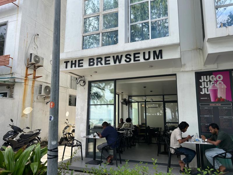 The Brewseum cafe frontage with customers at tables, a Drinks Menu board and a Jugo poster on the right