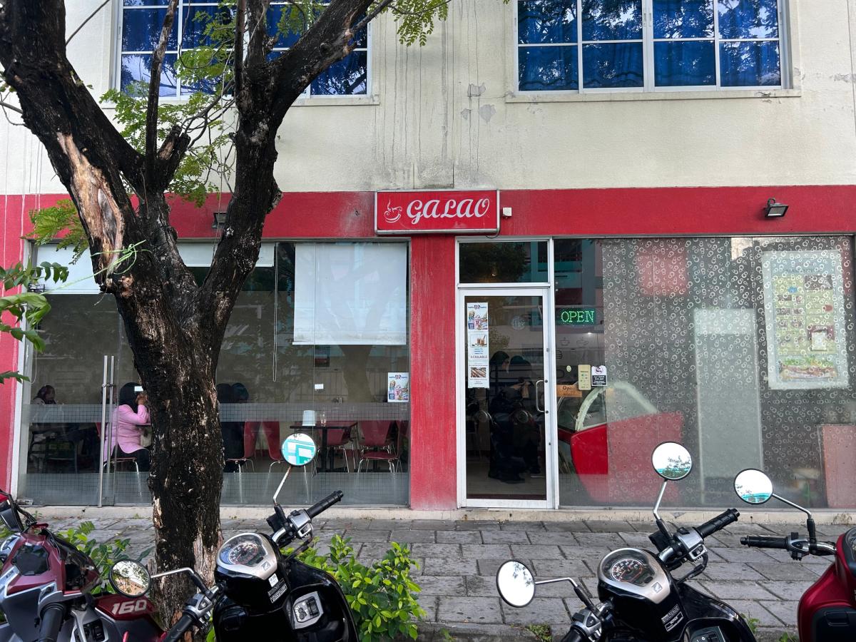 Red Galao cafe storefront with an Open sign, seen past a tree and parked scooters