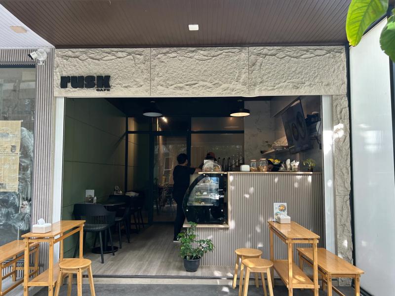 Rusk Cafe open-front counter with a pastry display, staff serving and wooden stools and tables on the pavement