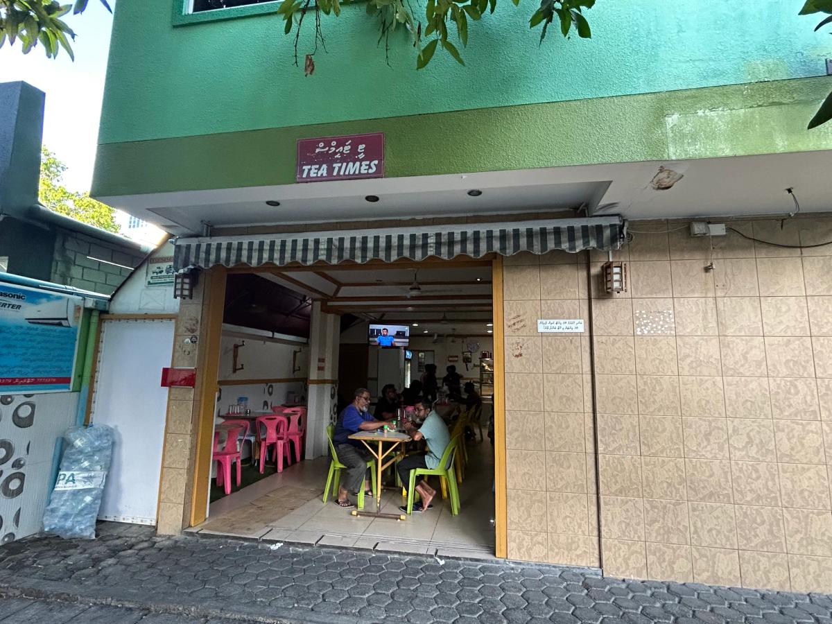Tea Times cafe entrance under a striped awning, with diners at plastic tables inside the open frontage