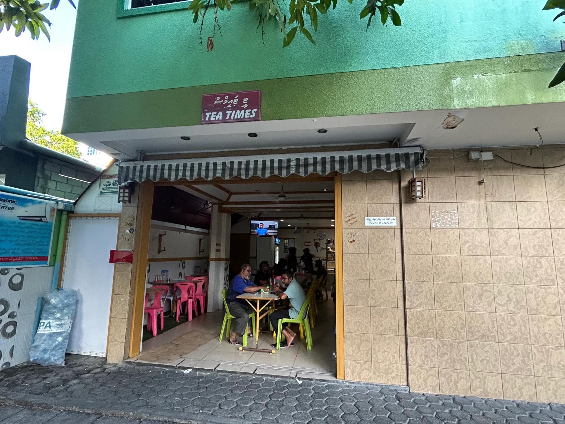 Tea Times cafe entrance under a striped awning, with diners at plastic tables inside the open frontage