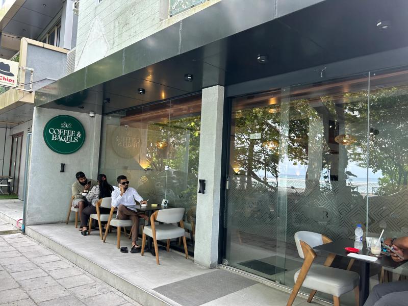 Coffee & Bagels' round green sign on a glass-walled cafe, with the seafront visible through the windows