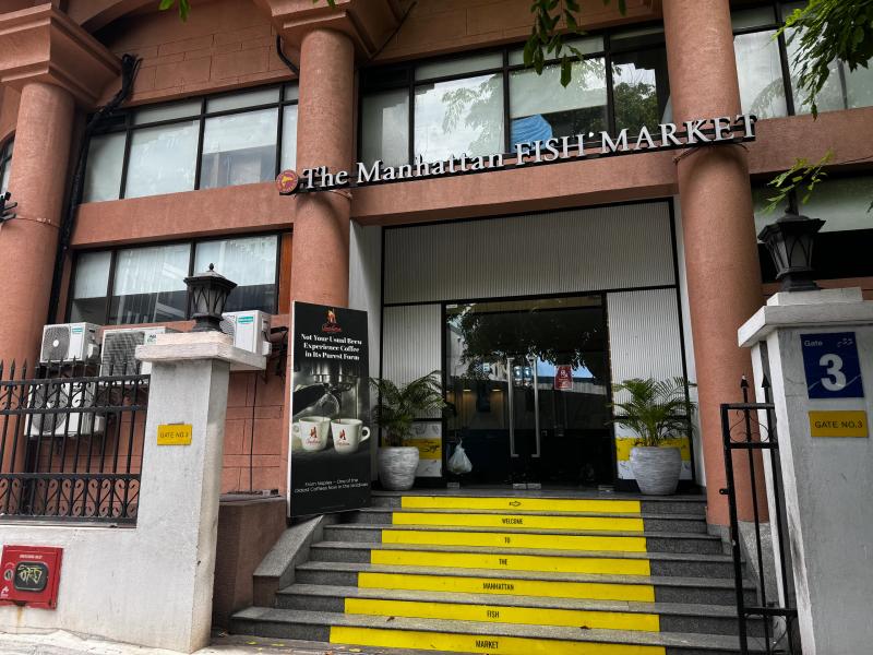 The Manhattan Fish Market entrance with raised columns and yellow stairs lettered Welcome To The Manhattan Fish Market