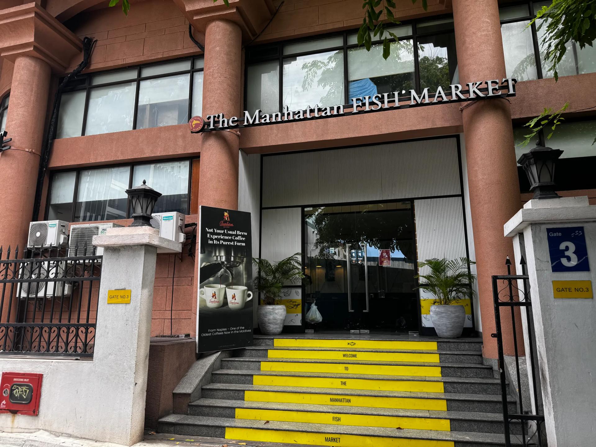 The Manhattan Fish Market entrance with raised columns and yellow stairs lettered Welcome To The Manhattan Fish Market