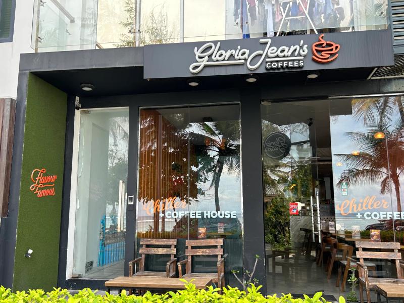 Gloria Jean's Coffees storefront with illuminated logo sign and wooden chairs out front