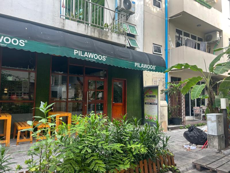 Green-awninged Pilawoos eatery with wooden benches outside and a menu board on the pavement