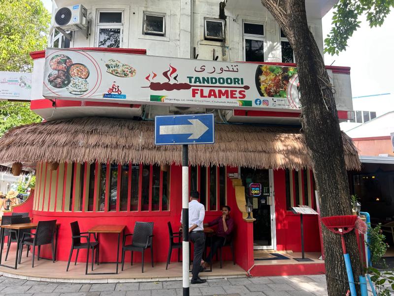 Tandoori Flames restaurant with food-photo billboard, thatched awning and red exterior seating on the street corner
