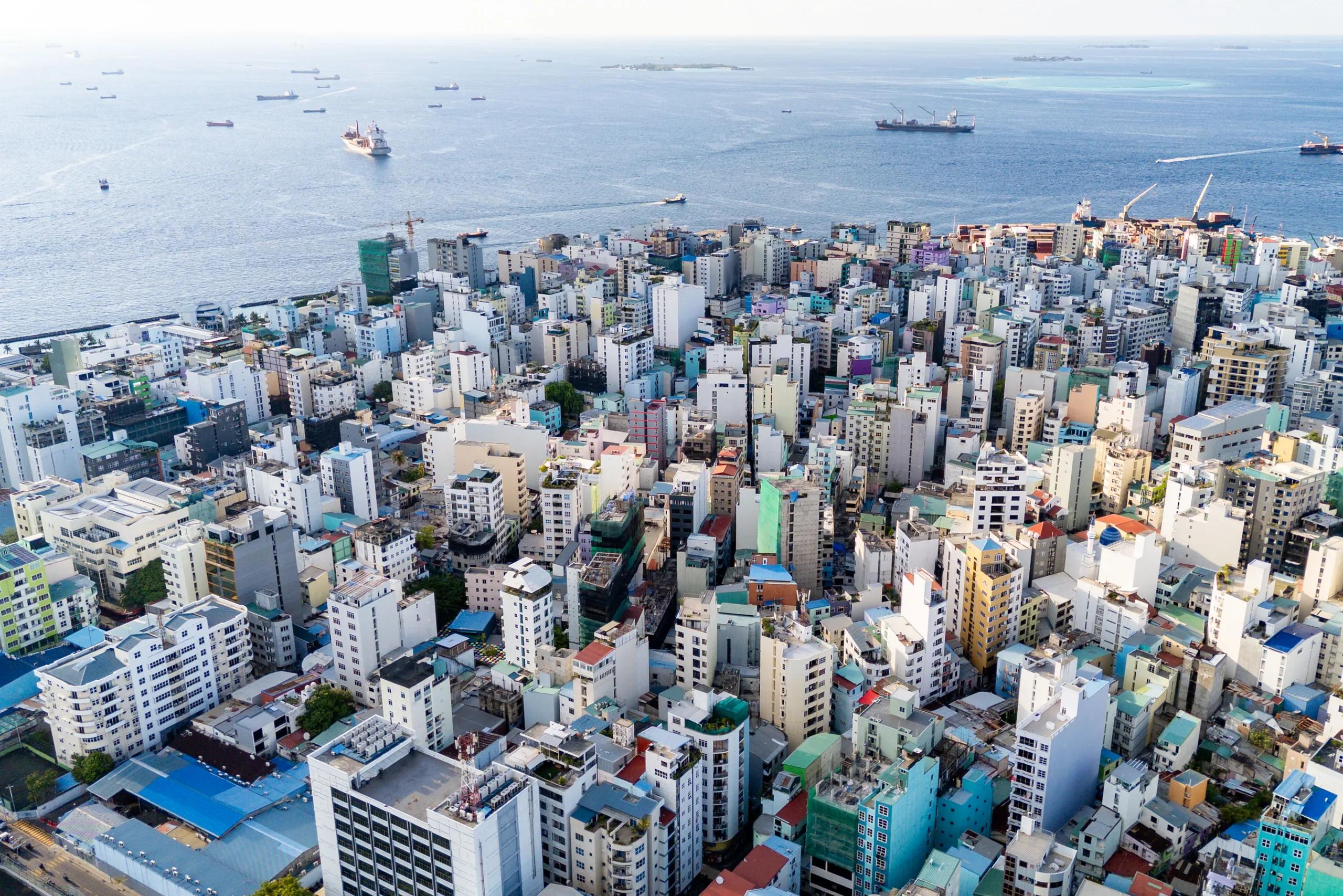 Aerial view over Malé's rooftops toward the sea, with cargo ships offshore