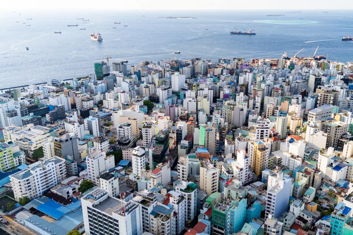 Drone view over the dense rooftops of Malé with cargo ships anchored offshore