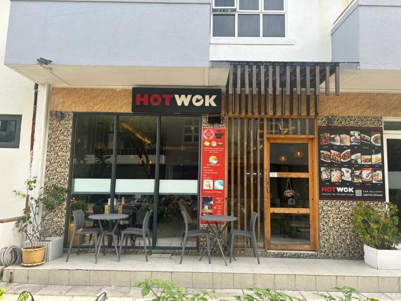 Hot Wok storefront with black signage, food menu posters and grey outdoor tables and chairs