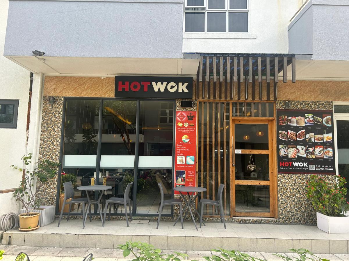 Hot Wok storefront with black signage, food menu posters and grey outdoor tables and chairs
