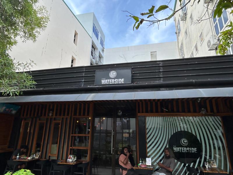The Waterside storefront with wooden-slat facade, swirl mural and customers seated at outdoor tables