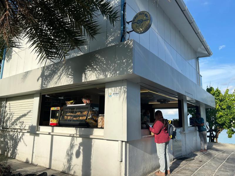 Why Not Hut beachside snack kiosk with a window counter and customers, palm trees and blue lagoon behind