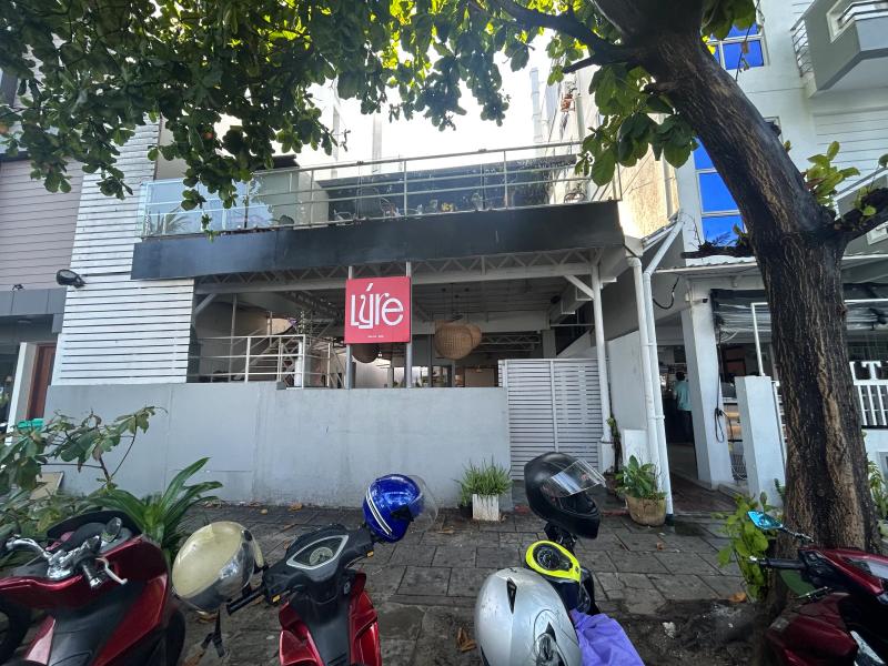 Two-storey Lyre building with a pink logo sign, balcony seating upstairs and scooters parked out front