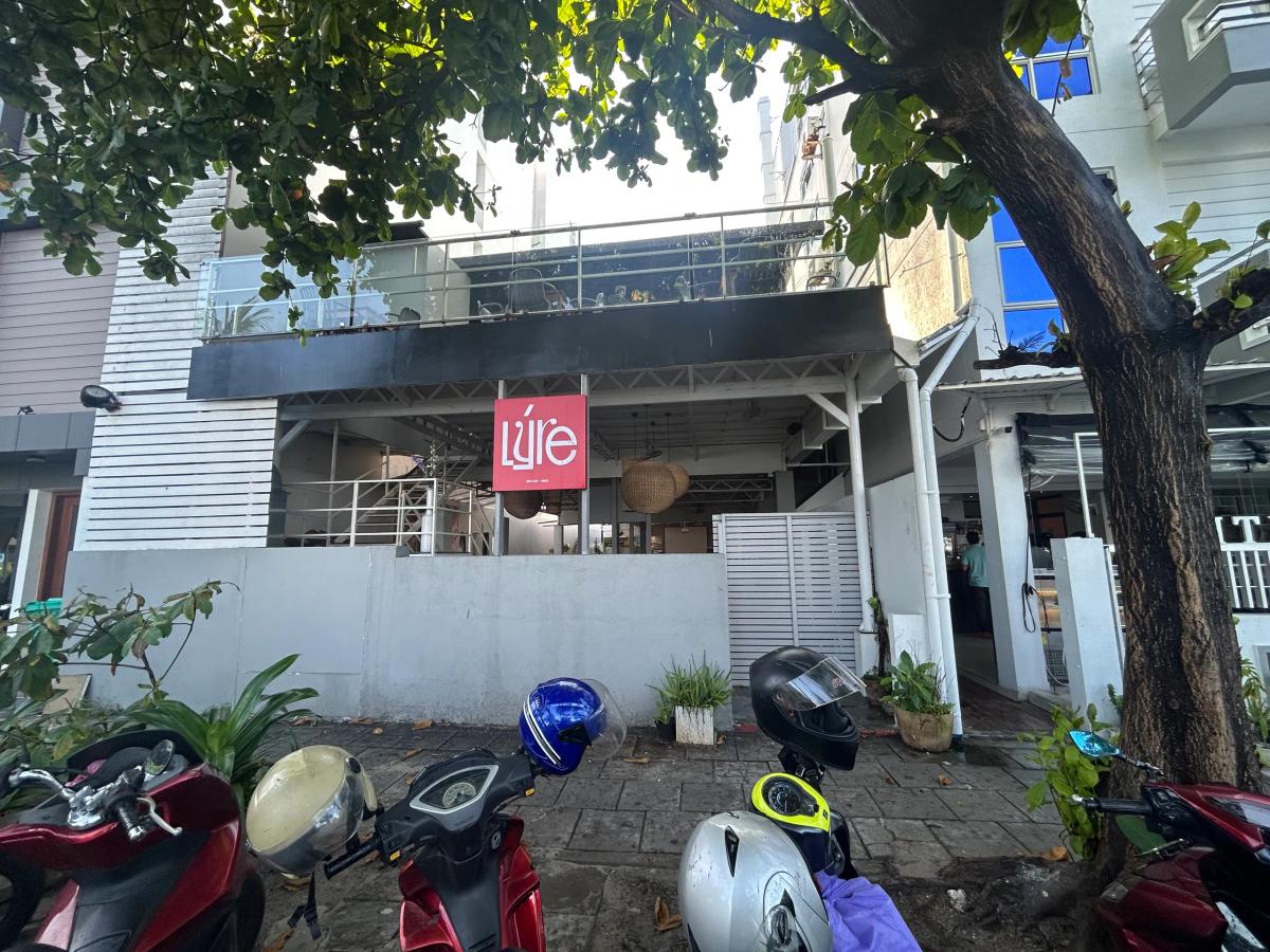 Two-storey Lyre building with a pink logo sign, balcony seating upstairs and scooters parked out front