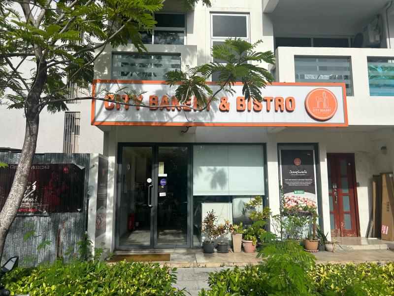 City Bakery & Bistro's orange-trimmed sign above a glass front lined with potted plants
