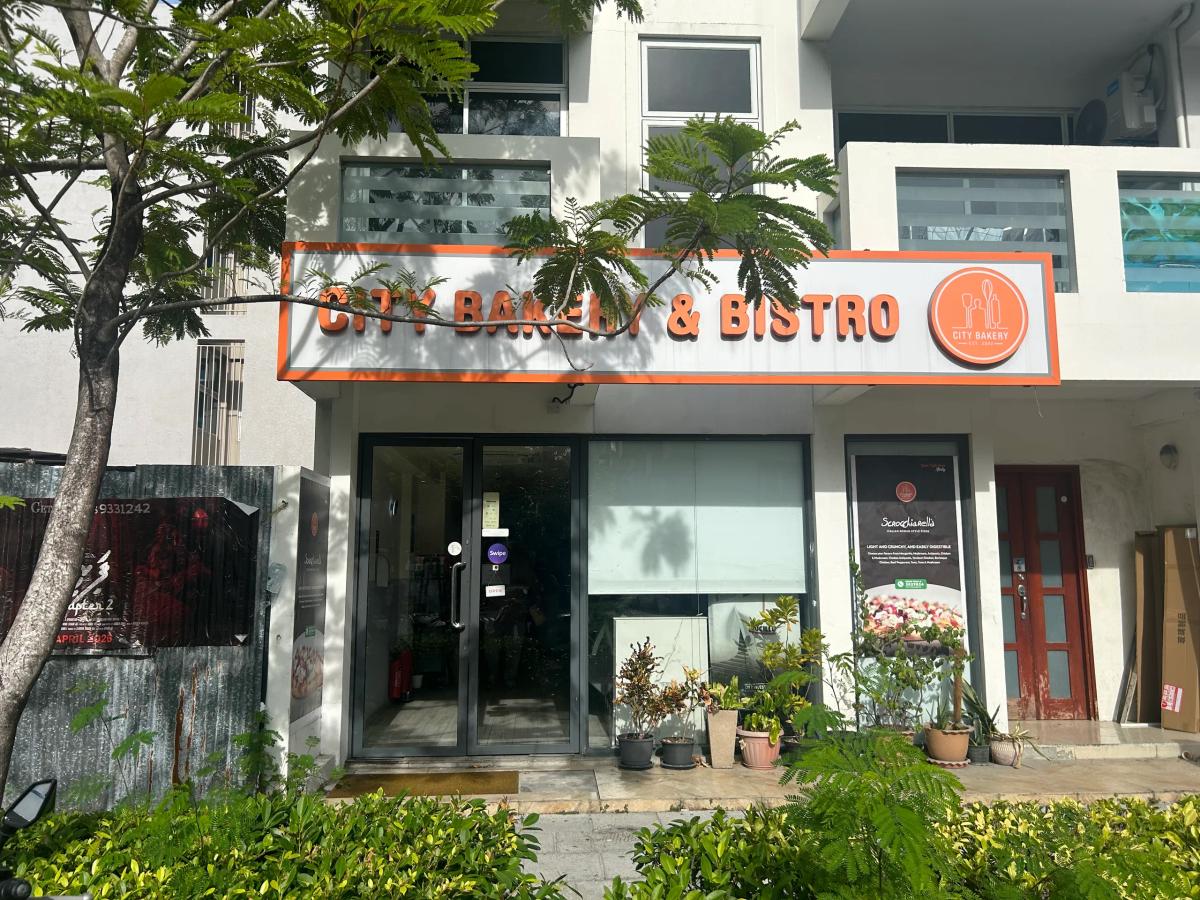 City Bakery & Bistro's orange-trimmed sign above a glass front lined with potted plants