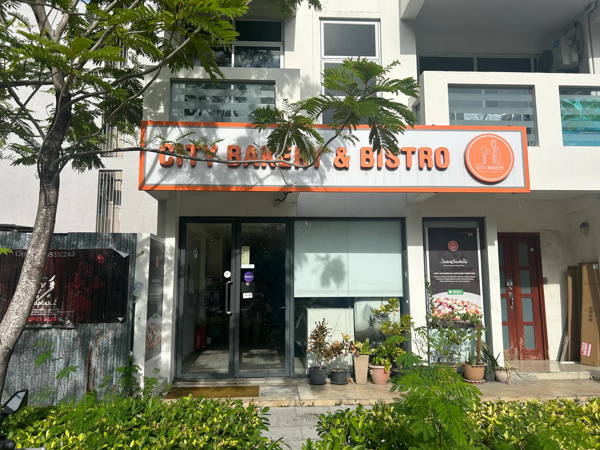 City Bakery & Bistro's orange-trimmed sign above a glass front lined with potted plants
