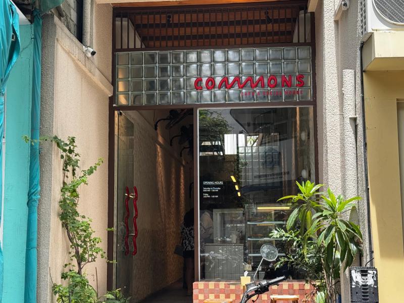 Narrow entrance to Commons Cafe & Social House with red neon-style sign and glass-block facade