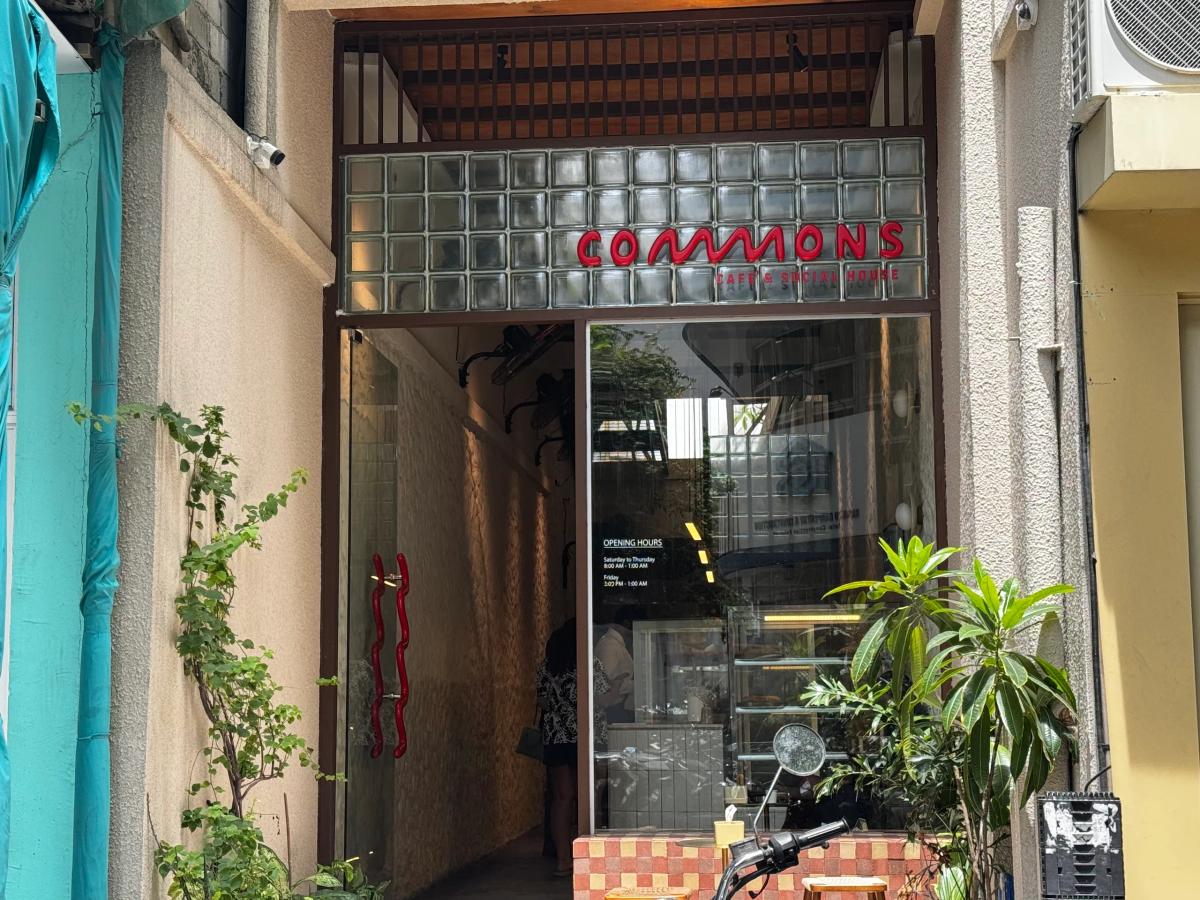 Narrow entrance to Commons Cafe & Social House with red neon-style sign and glass-block facade