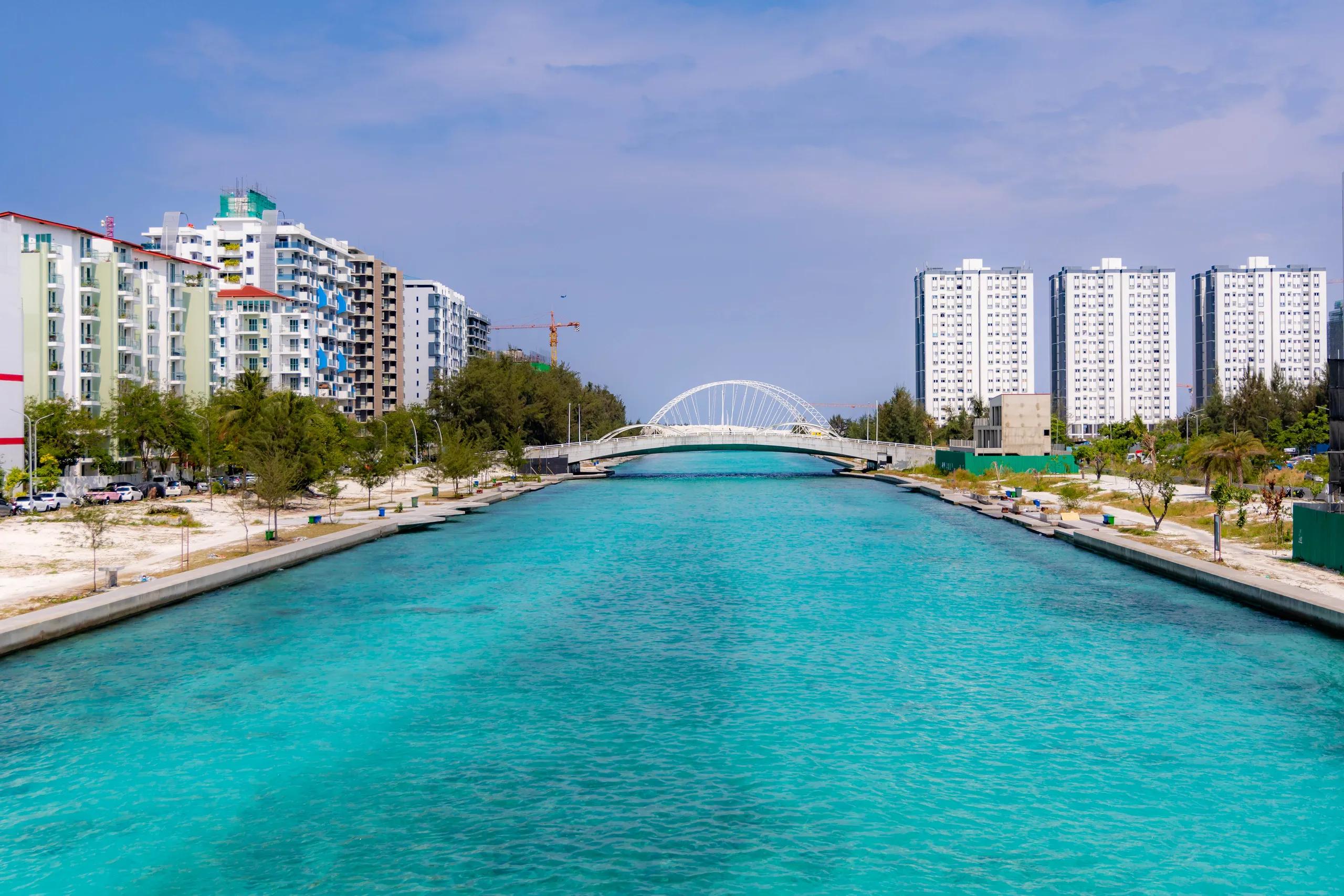 The turquoise Hulhumalé channel lined with promenades, with a white arch bridge ahead and housing towers on both banks