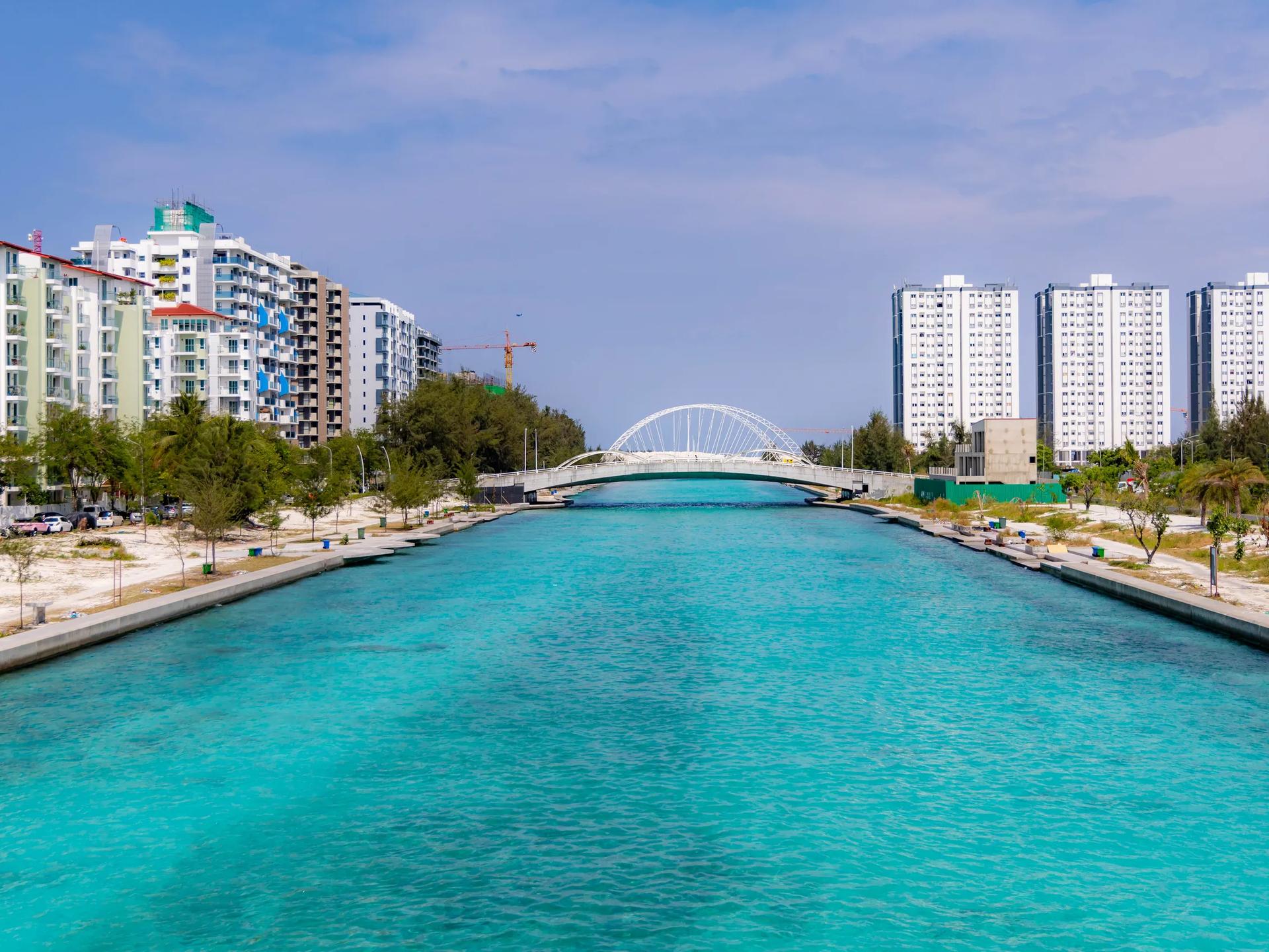 The turquoise Hulhumalé channel lined with promenades, with a white arch bridge ahead and housing towers on both banks
