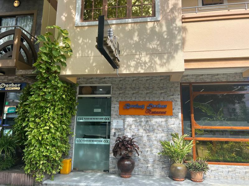 Bombay Darbar Restaurant's orange sign on a stone-clad wall, with potted plants flanking the entrance