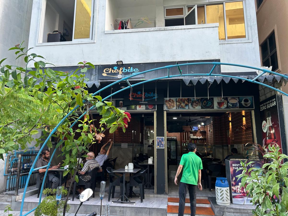 Chefbite's open-front eatery with a food display counter, framed by a blue arch over the pavement seating