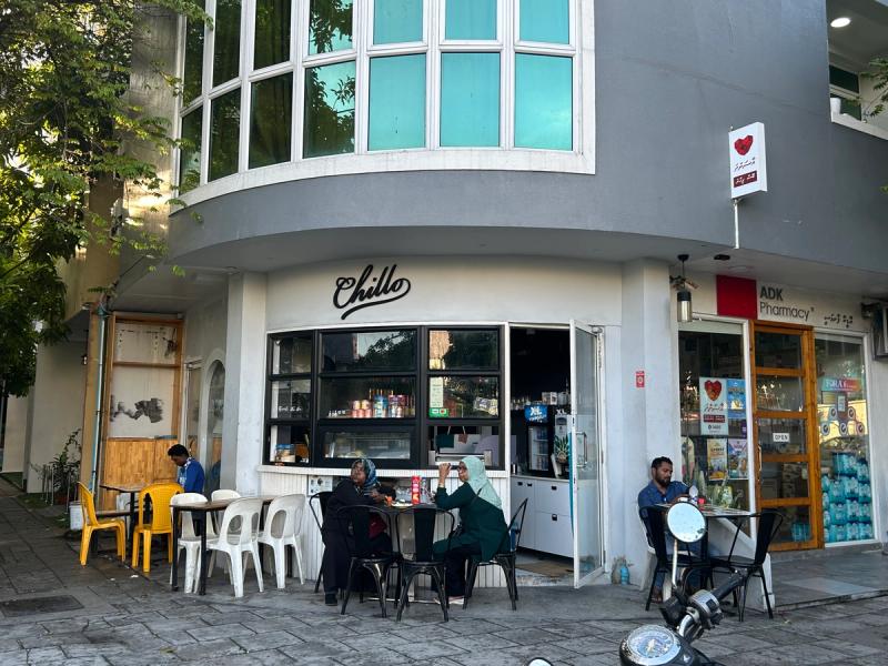 Chillo's script sign on a curved grey corner building, with tables outside next to ADK Pharmacy