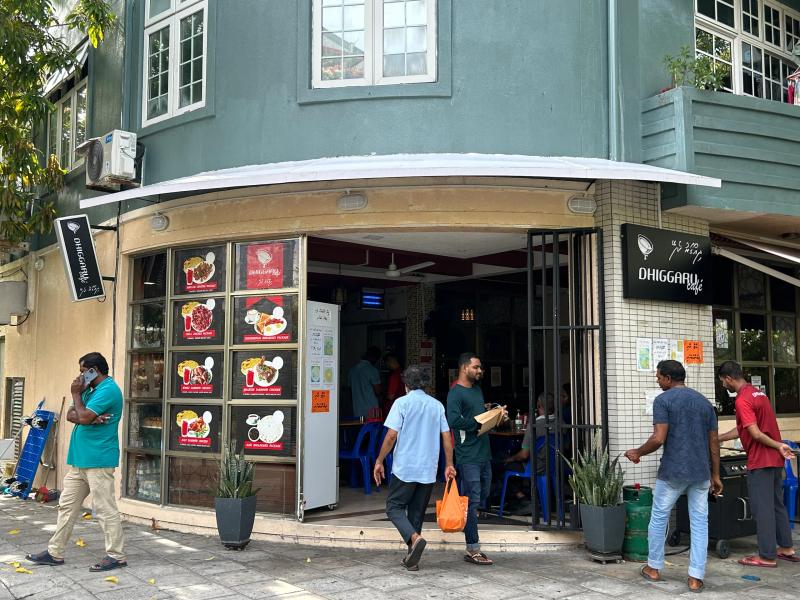 Corner entrance of Dhiggaru Cafe under a teal building, with food posters beside the open door