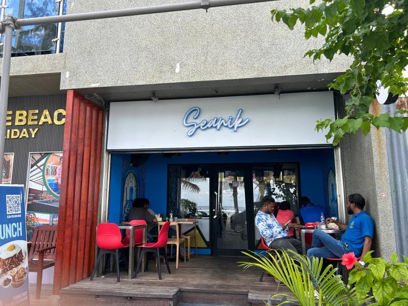 Seanik cafe with blue cursive sign and an open blue-painted front, diners seated at outdoor tables
