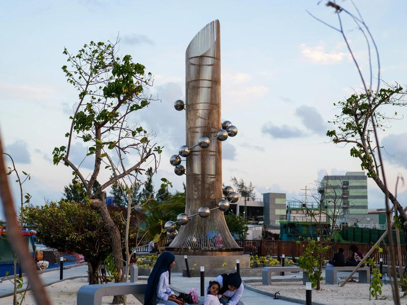 The steel Tsunami Monument, a spiral of metal spheres around a column of vertical rods, in a landscaped seafront plaza at dusk