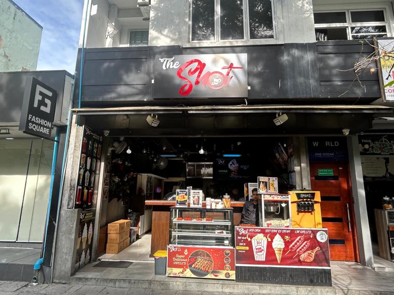 Open street-front counter at The Shot with popcorn machine, ice cream display and snack posters beside Fashion Square