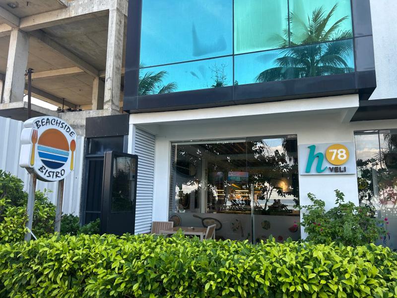 Beachside Bistro sign next to the glass-fronted ground floor of the h78 Veli hotel, behind a low hedge