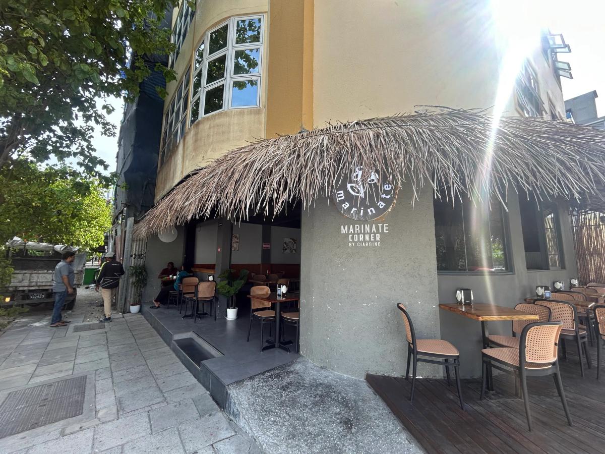 Marinate Corner by Giardino with a thatched awning over outdoor tables on a sunny Malé street corner