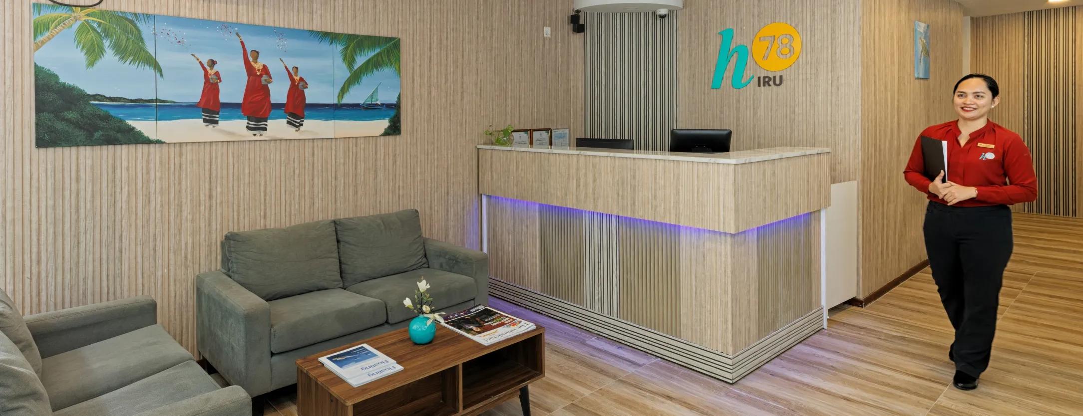 Reception of h78 Iru with wood-slat walls, the h78 Iru logo, a Maldivian beach painting and lobby sofas