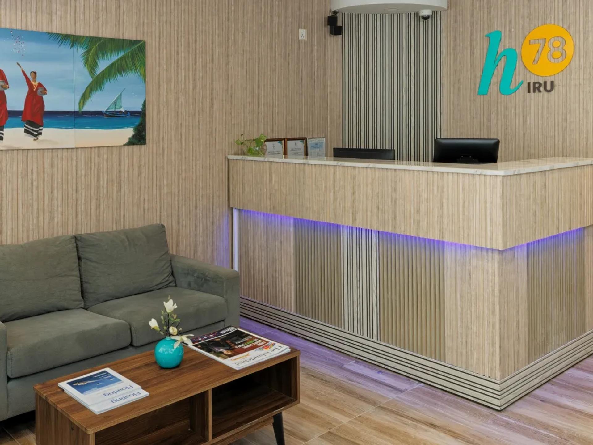 Reception of h78 Iru with wood-slat walls, the h78 Iru logo, a Maldivian beach painting and lobby sofas