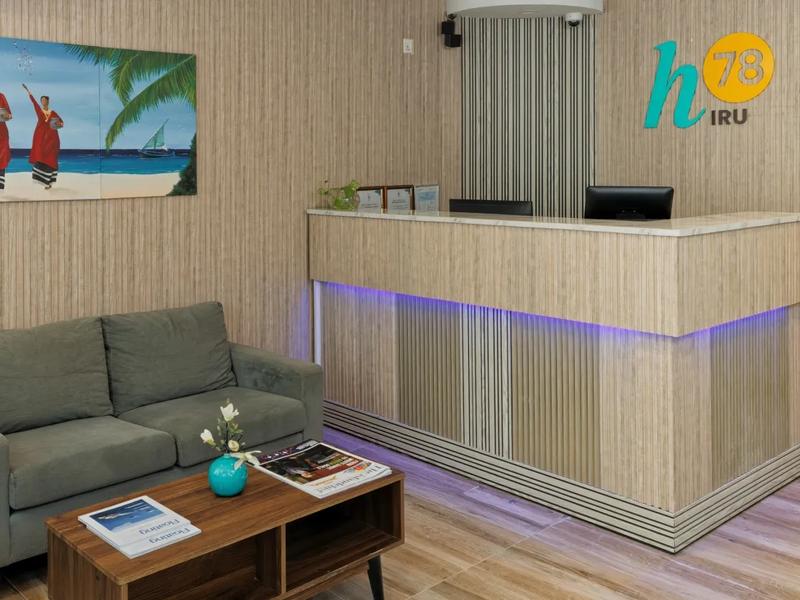 Reception of h78 Iru with wood-slat walls, the h78 Iru logo, a Maldivian beach painting and lobby sofas