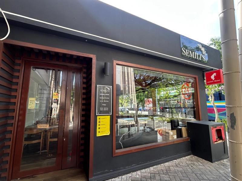 Semili's dark grey storefront with logo sign, large window, wooden door and an opening-hours notice board