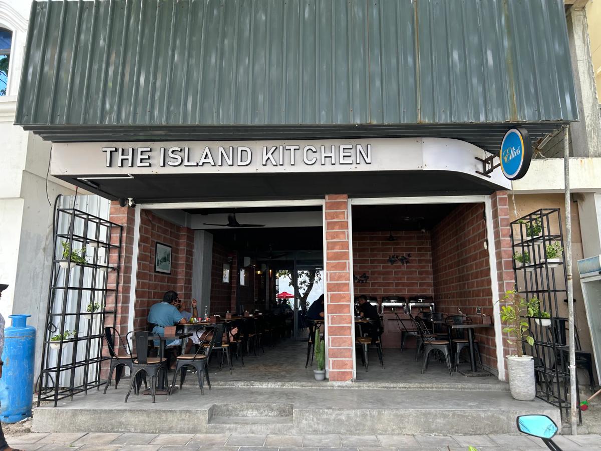 The Island Kitchen open-fronted restaurant with brick interior walls, metal chairs and diners under a green awning