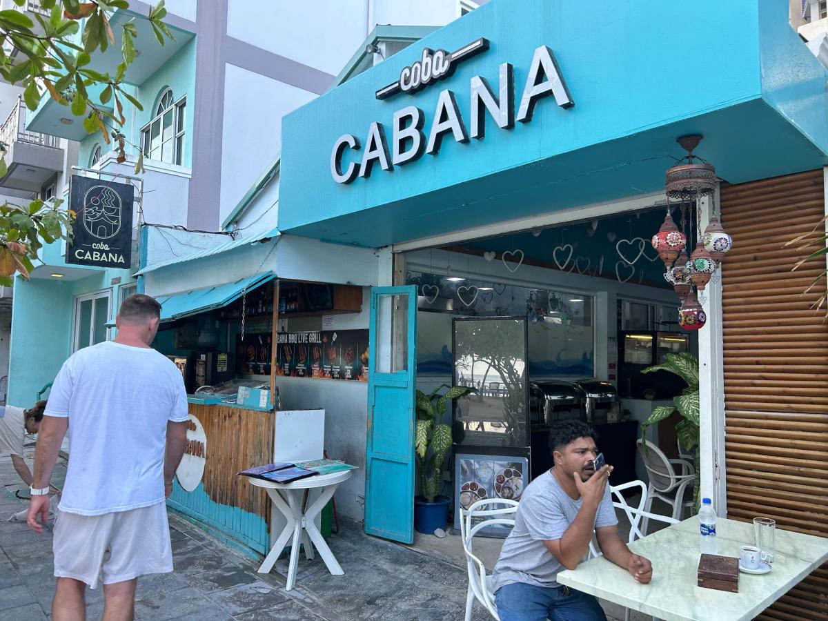 Turquoise open-front Coba Cabana with its name above the awning, hanging lanterns and street-side tables