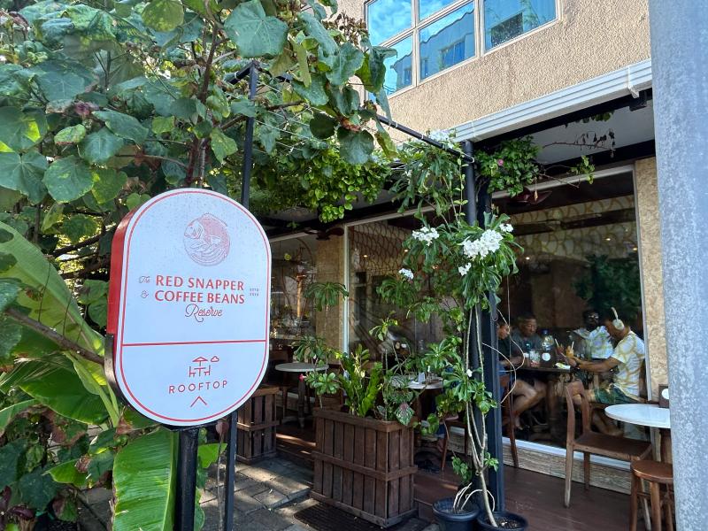 Red Snapper & Coffee Beans rooftop sign beside a leafy outdoor terrace with diners seated by glass windows
