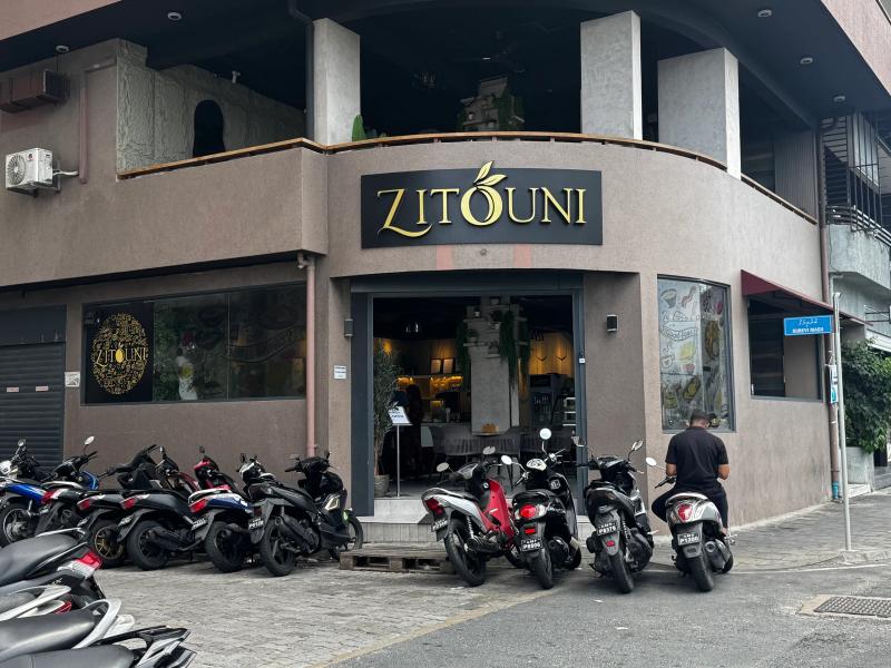 Corner ZITOUNI restaurant with black-and-gold sign and open entrance, rows of motorbikes parked along the street
